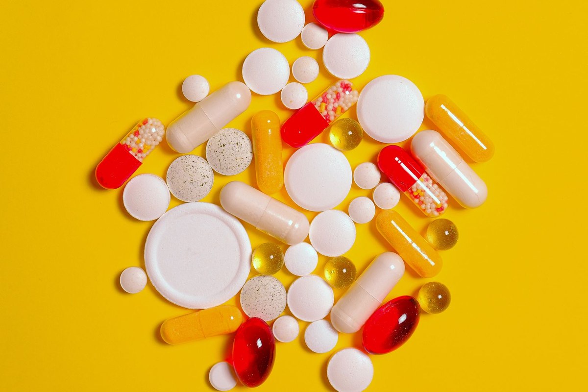 Assorted tablets, capsules, and softgels scattered on a bright yellow background