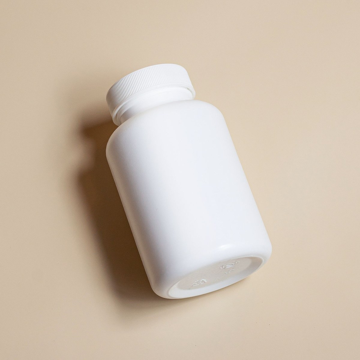 Unbranded white plastic supplement bottle with ribbed cap on a beige background